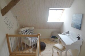 Ein Zimmer mit schrägem Dach, einem Fenster, einem Schreibtisch mit Stuhl, einem Bett und einer Wand mit einer Zeichnung.
