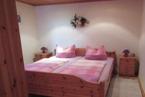 Ein Bett mit Holzbettgestell, rosa Bettwäsche, zwei Nachttische und eine Wanddekoration.