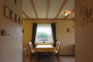 Ein Essbereich mit Tisch und Stühlen, einem Fenster mit Vorhängen und einer Decke mit Holzbalken.