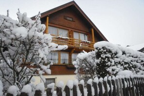 Ein zweistöckiges Holzhaus mit Balkon, umgeben von schneebedeckten Bäumen.