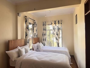 Una habitación con dos camas, cabecero de madera y una ventana con cortinas decorativas.