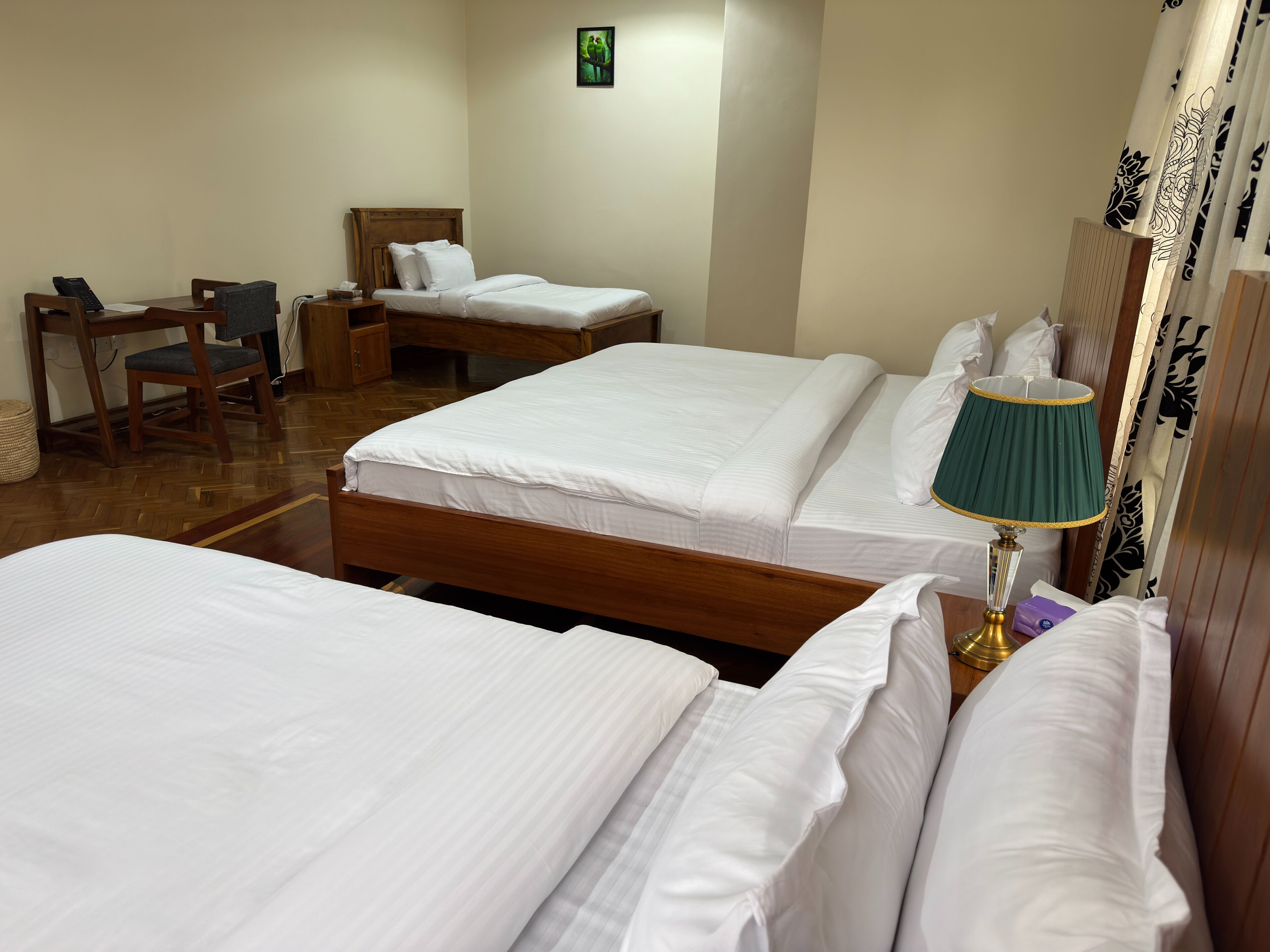 Habitació d'hotel amb dos llits, una taula de treball, una cadira, una tauleta de nit i una làmpada.