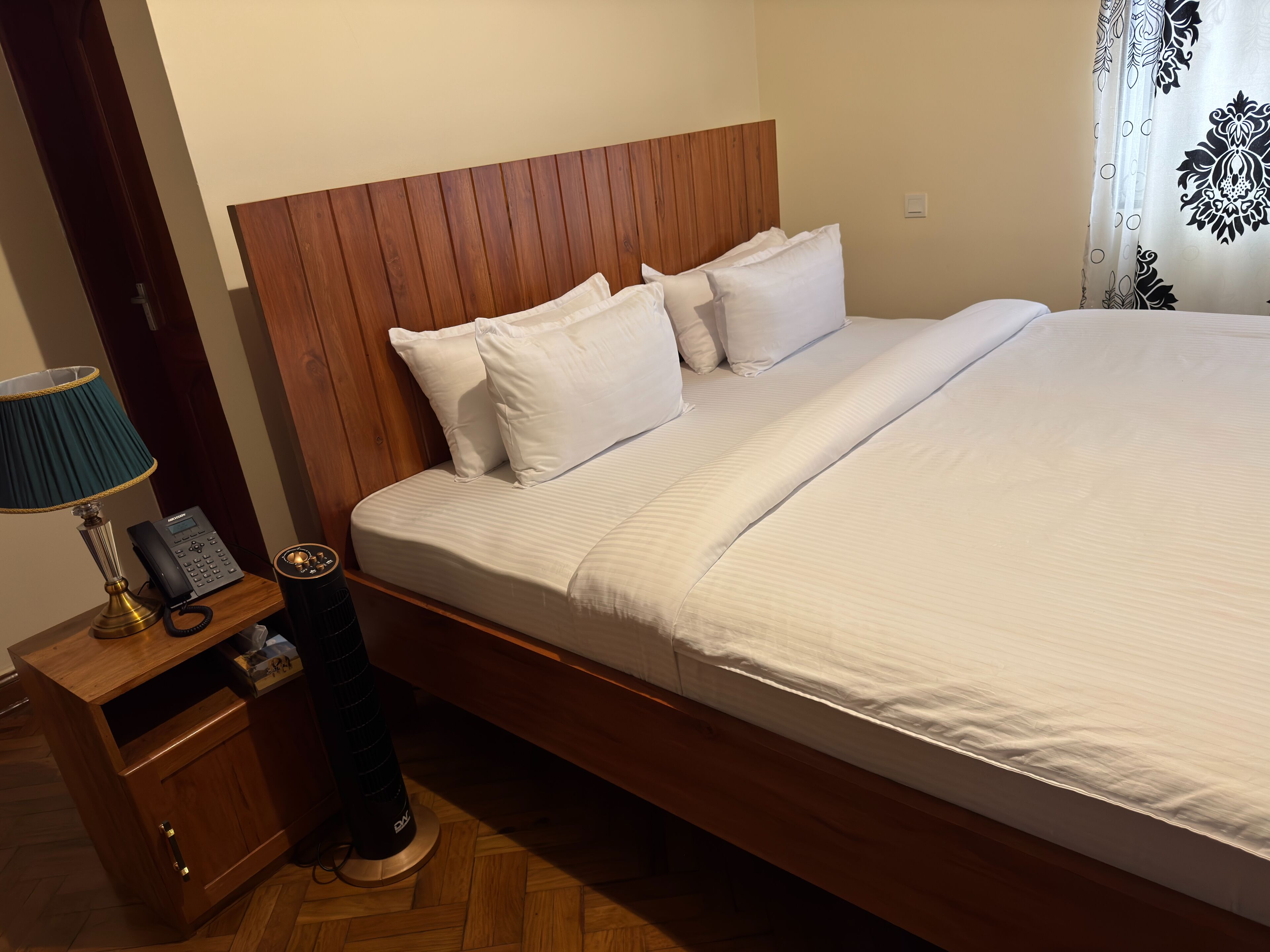A neatly made bed with a wooden headboard, a bedside table with a lamp, and a telephone.