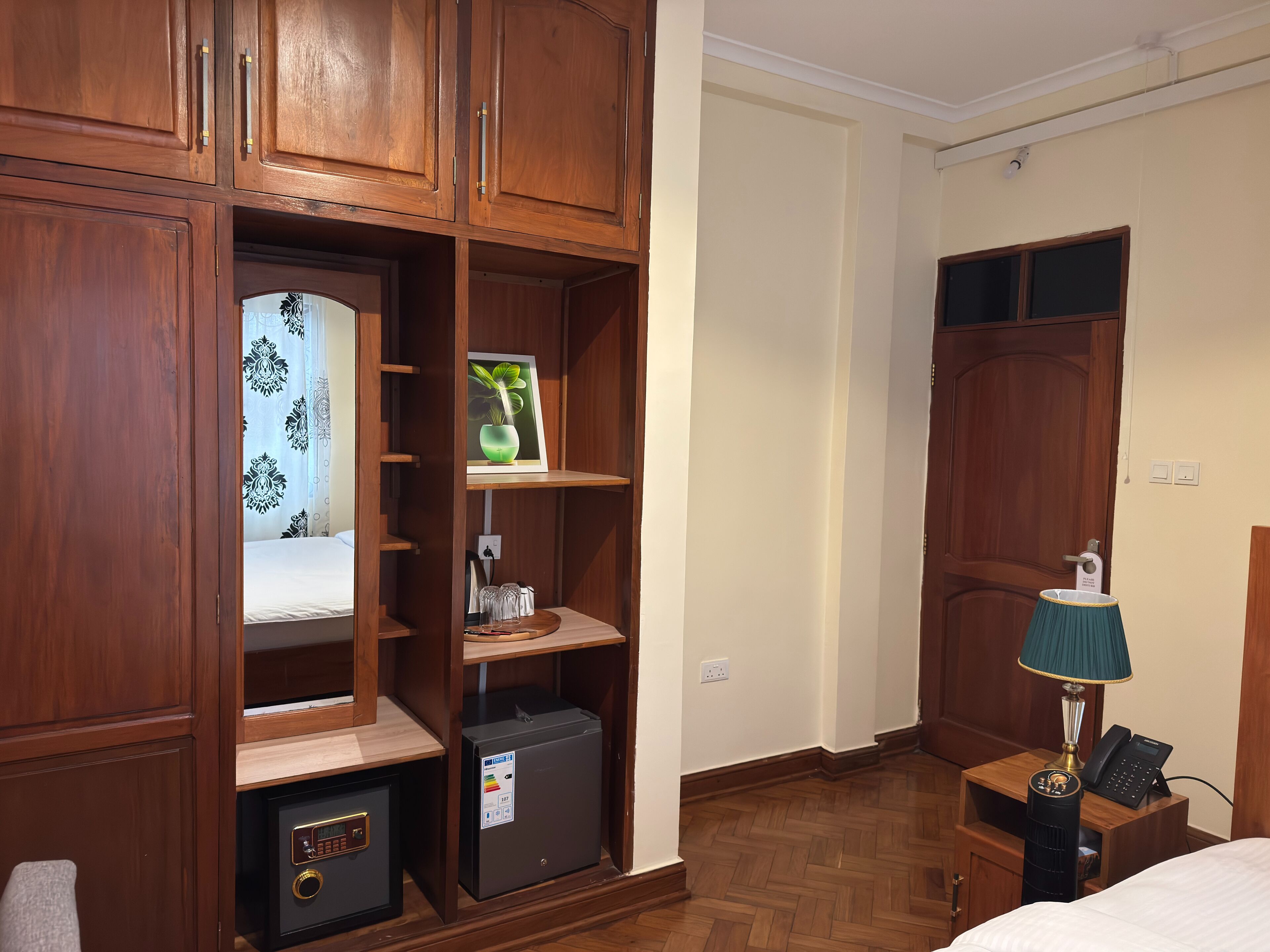 A hotel room with wooden cabinetry, a bed, a nightstand with a lamp, and a safe.
