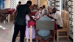 Un comedor con sillas y mesas de madera, suelo de baldosas y cortinas estampadas.