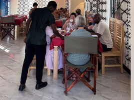 A dining area with wooden chairs and tables, a tiled floor, and patterned curtains.