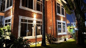 Un edificio de ladrillo de dos pisos con ventanas amplias, césped cuidado y una palmera.