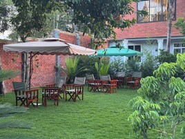 An outdoor seating area with chairs and umbrellas, surrounded by greenery and a brick wall.
