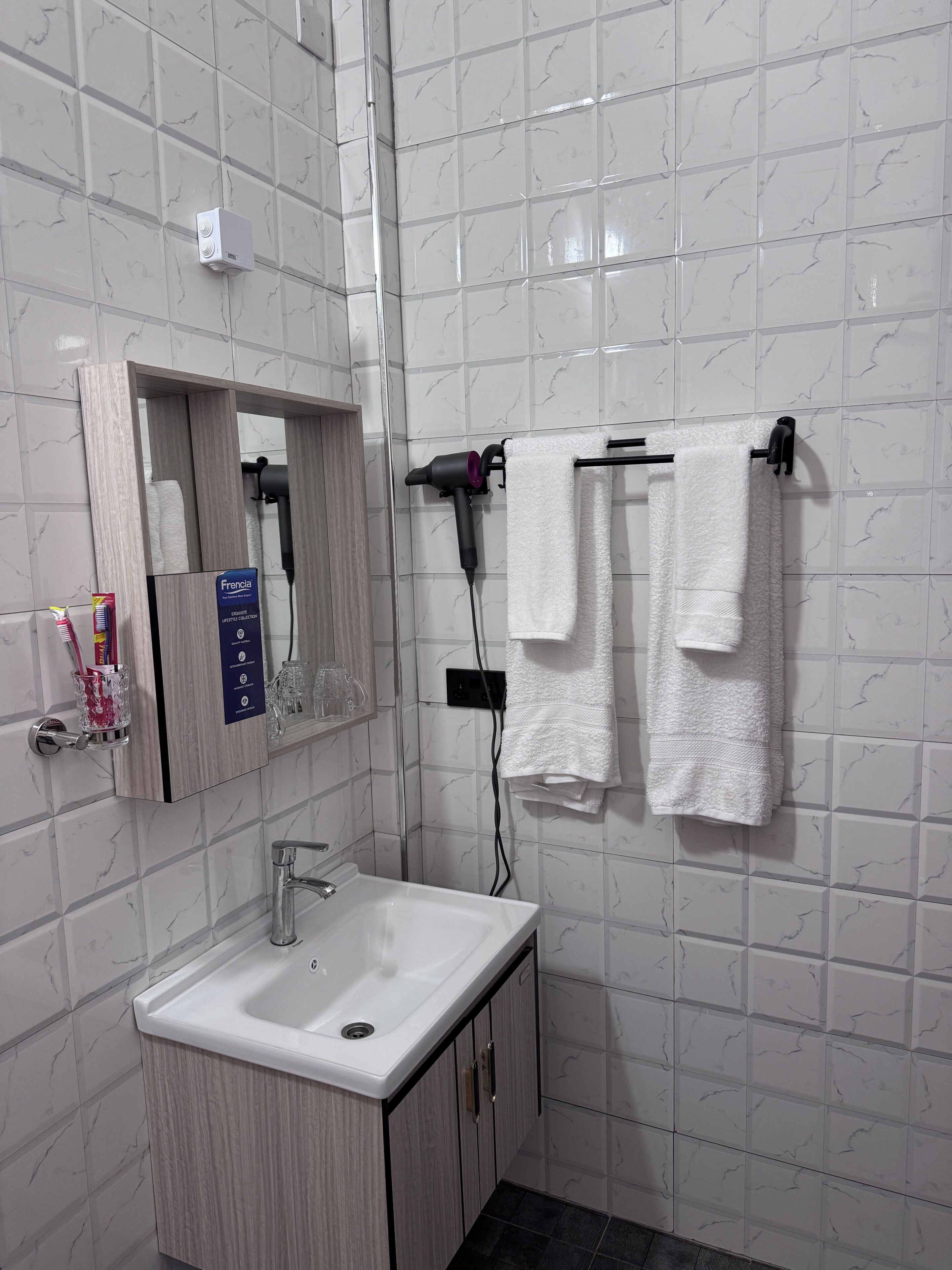 Un baño con lavamanos, espejo, perchero para toallas y artículos de aseo.