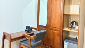 Una habitación con escritorio de madera, una silla, armario y una pequeña kitchenette.