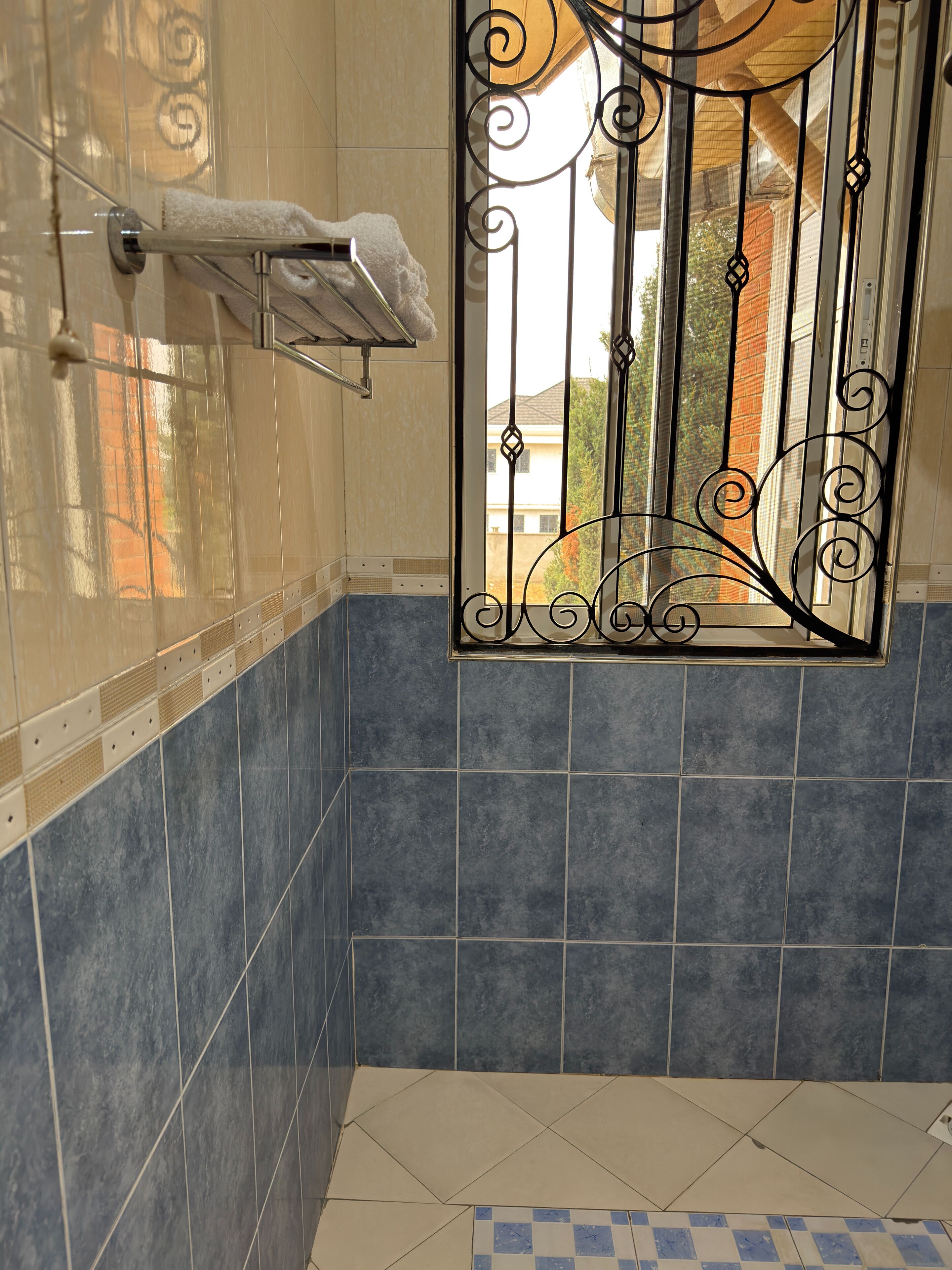Un baño con ducha, paredes de azulejos, un perchero y una reja decorativa de metal.