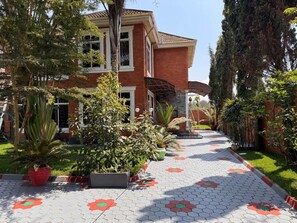 Una casa de dos pisos con fachada de ladrillo, un porche cubierto y un camino pavimentado con baldosas hexagonales.