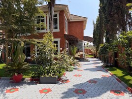 A two-story house with a brick exterior, a covered porch, and a paved pathway with hexagonal tiles.