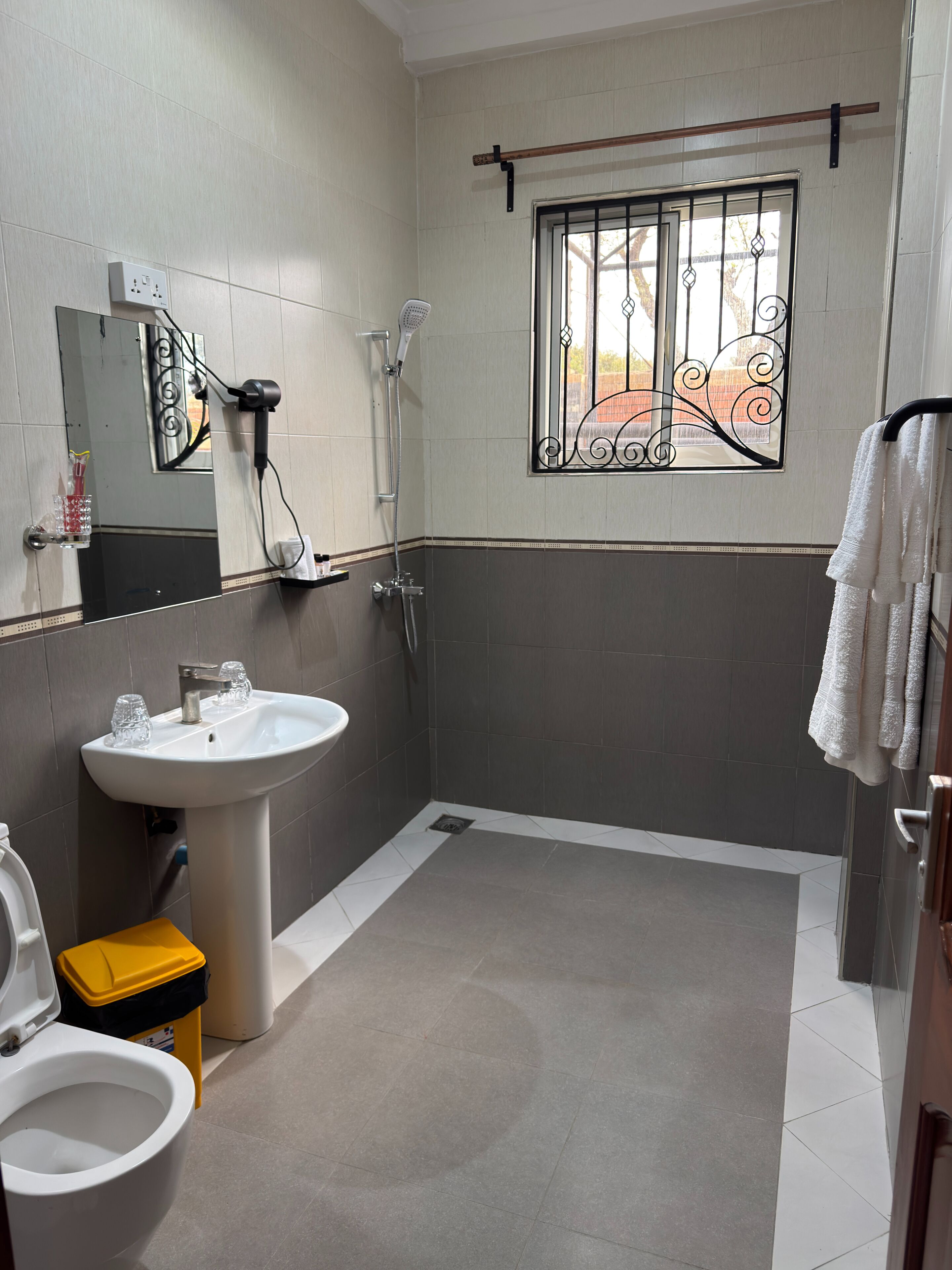 A bathroom with a sink, toilet, shower, and a window with decorative iron bars.