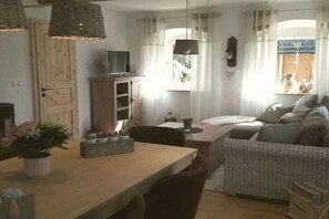 A cozy living room with a sofa, a dining table, and a TV on a wooden cabinet. - Holiday home Chalet Bianca (Bayern - Grafengehaig)