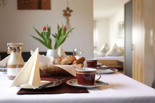 Ein Frühstückstisch für zwei Personen, gedeckt mit Brot, Gebäck und einer Tasse.