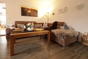 Ein Wohnzimmer mit einem braunen Sofa, einem Holztisch, einer weißen Vase und einer Weinflasche.