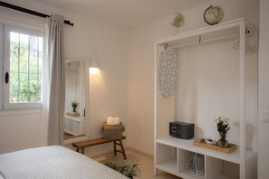 Ein Schlafzimmer mit Bett, Nachttisch, Spiegel, einer Kommode mit Dekoration und einem Fenster mit Vorhängen.
