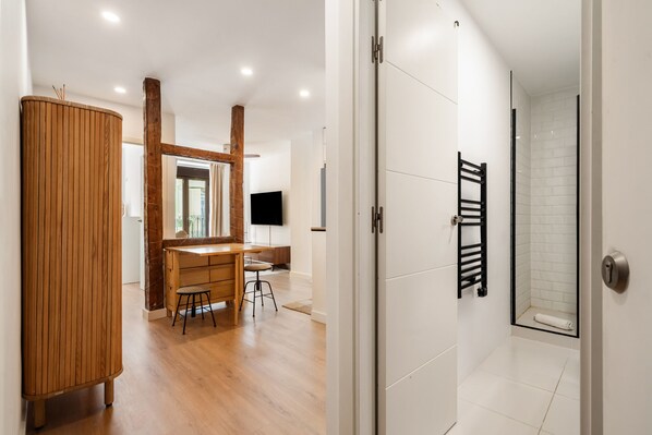Ein modernes Interieur mit einem Holzkabinett, einem Schreibtisch mit Hocker, einem Duschbereich und einem an der Wand montierten Fernseher.