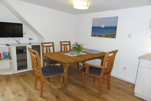 Ein Essbereich mit Holztisch und -stühlen, einem Segelboot-Gemälde an der Wand und einem Fernseher auf einem Schrank.