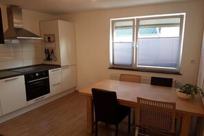 A kitchen with white cabinets, a black oven, and a dining table with chairs. - Holiday apartment in Werbach with barbecue (Werbach)