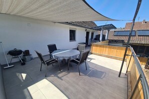 A patio with a table and chairs, a barbecue grill, and a wooden deck. - Holiday apartment in Werbach with barbecue (Werbach)
