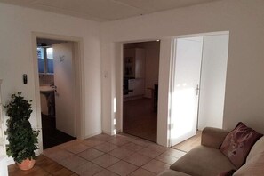 A living room with a beige sofa, a potted plant, and a door leading to a kitchen. - Holiday apartment in Werbach with barbecue (Werbach)