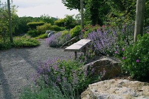A gravel path with a stone bench and a signpost in a garden with purple flowers and greenery. - Apartment in Obervolkach with swimming pool (Obervolkach)
