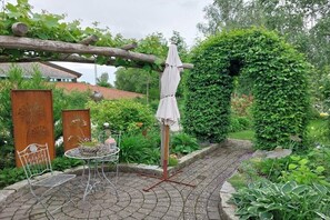 Eine Gartenpatio mit Tisch und Stühlen, einer Pergola und einem weißen Sonnenschirm.