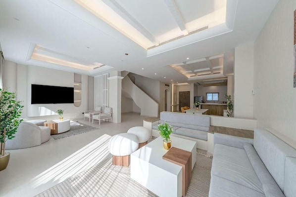 A modern living room with a flat-screen TV, white sofas, a coffee table, and a staircase leading to another level.