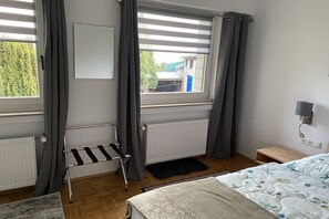 Ein Schlafzimmer mit Bett, Heizkörper, Fenster mit Vorhängen und einem kleinen Nachttisch.