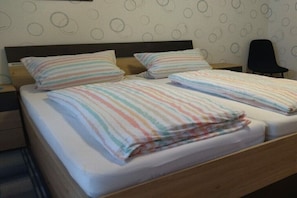 Un letto matrimoniale con lenzuola a righe, una testiera in legno e una sedia in una stanza con carta da parati decorata.