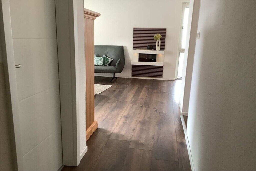 Ein Flur mit Holzboden, einem grünen Sofa und einem an der Wand befestigten Regal mit Dekoration.