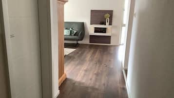 Ein Flur mit Holzboden, einem grünen Sofa und einem an der Wand befestigten Regal mit Dekoration.
