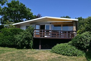Ein modernes, zweistöckiges Haus mit Balkon, umgeben von üppigem Grün.