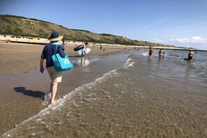 Ein Strand mit Menschen, die spazieren gehen und schwimmen, einem klaren Himmel und einer hügeligen Landschaft im Hintergrund.