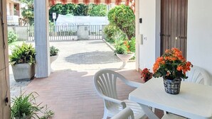 A covered patio with a table and chairs, potted plants, and a view of a garden and buildings in the background. - Casa degli Orti in Venice (Dolo)