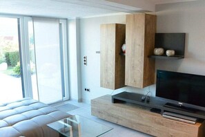 A modern living room with a sofa, a flat-screen TV, wooden cabinets, and a sliding glass door. - Holiday apartment with 1 bedroom (Friedrichroda)