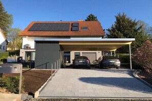 Ein modernes Haus mit Solardach, zwei Autos auf der Auffahrt und einer Garage mit Überdachung.