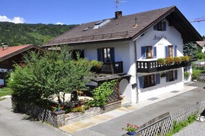 Ein traditionelles Gebäude im alpinen Stil mit Balkon, Holzzaun und einem Garten mit Topfpflanzen.