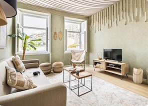 Ein Wohnzimmer mit Sofa, Sessel, Couchtisch, TV-Schrank und einem großen Fenster.