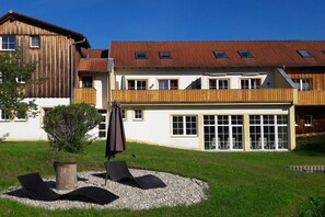 Ein mehrstöckiges Gebäude mit einem geneigten Dach, großen Fenstern und einem grünen Innenhof mit Außenbestuhlung.