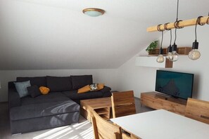 Uma sala de estar moderna com sofá, TV, mesa de jantar de madeira e luminárias pendentes.