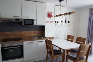 Cozinha moderna com armários brancos, bancada de madeira, forno embutido, micro-ondas e um espaço de refeições com mesa branca e cadeiras de madeira.