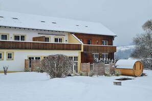 Um edifício de dois andares com fachada de madeira, telhado coberto de neve e um barril em primeiro plano.