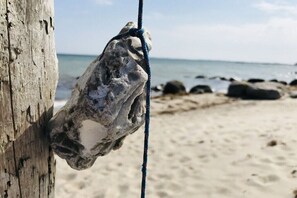 A rock tied to a wooden post on a beach with a clear sky and ocean in the background. - Beach Villa 33 Sea View (Großenbrode)