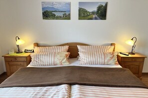 Ein Doppelbett mit gestreifter Bettwäsche, zwei Nachttische mit Lampen, ein Holz-Kopfteil und zwei gerahmte Bilder an der Wand.
