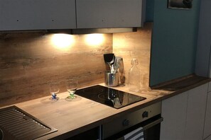 Eine Küche mit einer Holzausziehtheke, einem Induktionskochfeld, einer Spüle und einer Spritzschutzwand.