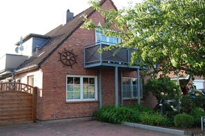Ein Ziegelhaus mit Balkon, einem Holztor und einem Garten mit verschiedenen Pflanzen.