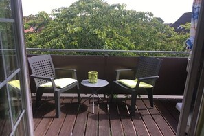 Ein Balkon mit zwei Stühlen und einem kleinen Tisch, mit Blick auf eine üppige Grünfläche.